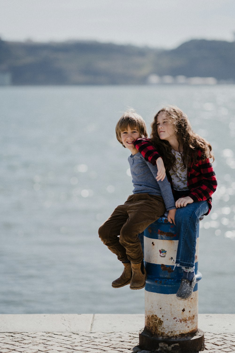 woman and child sits on white and blue metal capstan in dock