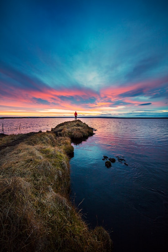 man stands on end of dike watching setting sun over sea in Mývatn Iceland