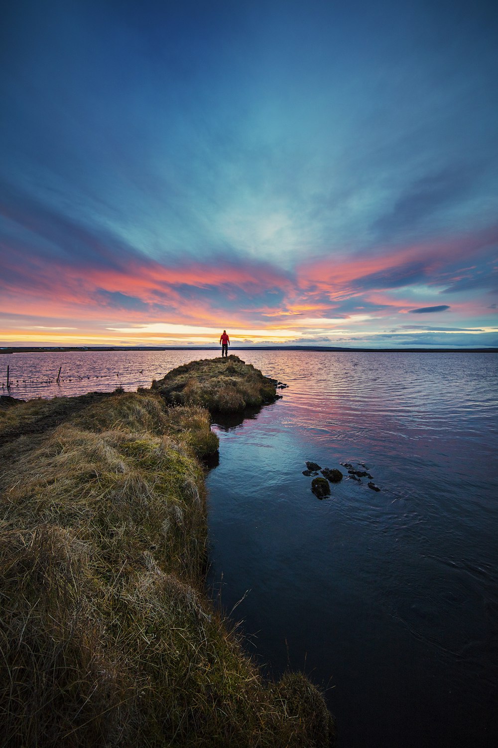 man stands on end of dike watching setting sun over sea