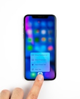 A smartphone displaying a blurred screen with colorful app icons and a menu with options for reading list, bookmarks, private tab, and new tab. A person's finger is pressing on the screen, interacting with the menu.