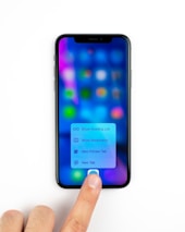 A smartphone displaying a blurred screen with colorful app icons and a menu with options for reading list, bookmarks, private tab, and new tab. A person's finger is pressing on the screen, interacting with the menu.