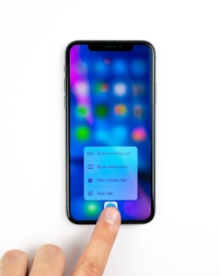A smartphone displaying a blurred screen with colorful app icons and a menu with options for reading list, bookmarks, private tab, and new tab. A person's finger is pressing on the screen, interacting with the menu.