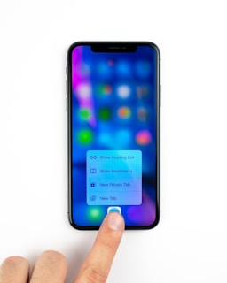 A smartphone displaying a blurred screen with colorful app icons and a menu with options for reading list, bookmarks, private tab, and new tab. A person's finger is pressing on the screen, interacting with the menu.