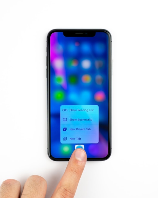 A smartphone displaying a blurred screen with colorful app icons and a menu with options for reading list, bookmarks, private tab, and new tab. A person's finger is pressing on the screen, interacting with the menu.
