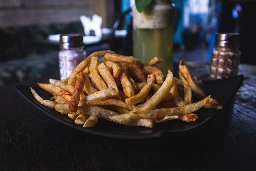 batatas fritas na placa de cerâmica preta no topo da mesa de madeira