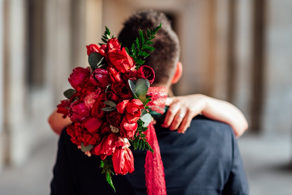 man hugging woman carrying red flower bouquet
