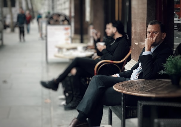 A casual yet polished look showing a man in a fitted shirt and chinos, seated at a café table.