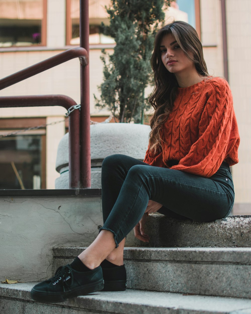 mujer con suéter naranja de cuello redondo sentada en la escalera