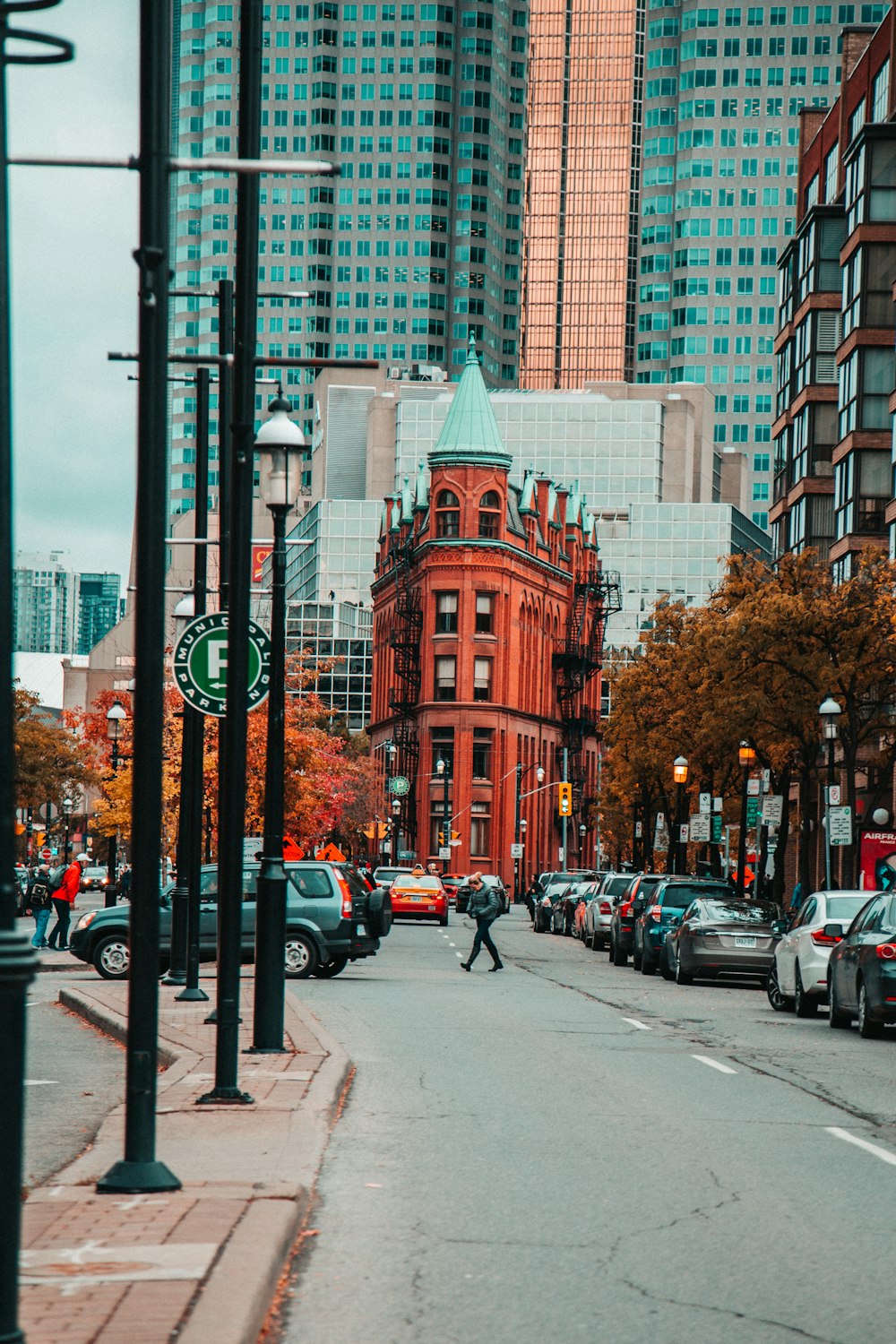 person crossing the road with parked cars beside the red building during daytime