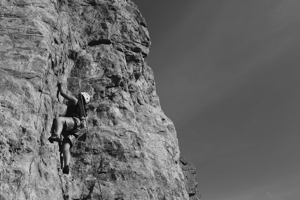 grayscale photography of man climbing rock