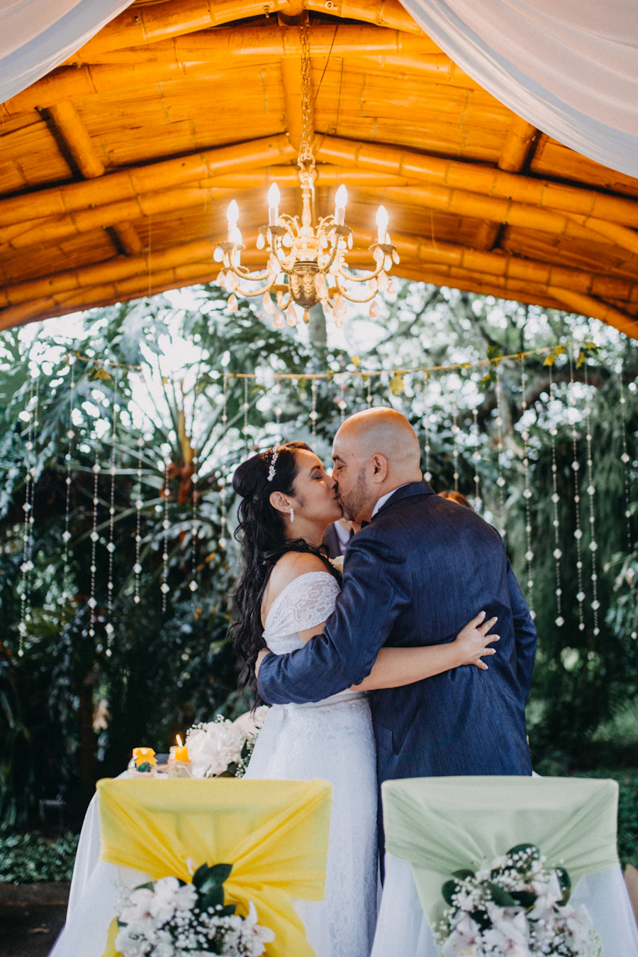 Newlywed couple kissing under an elegant chandelier at a Colombian reception