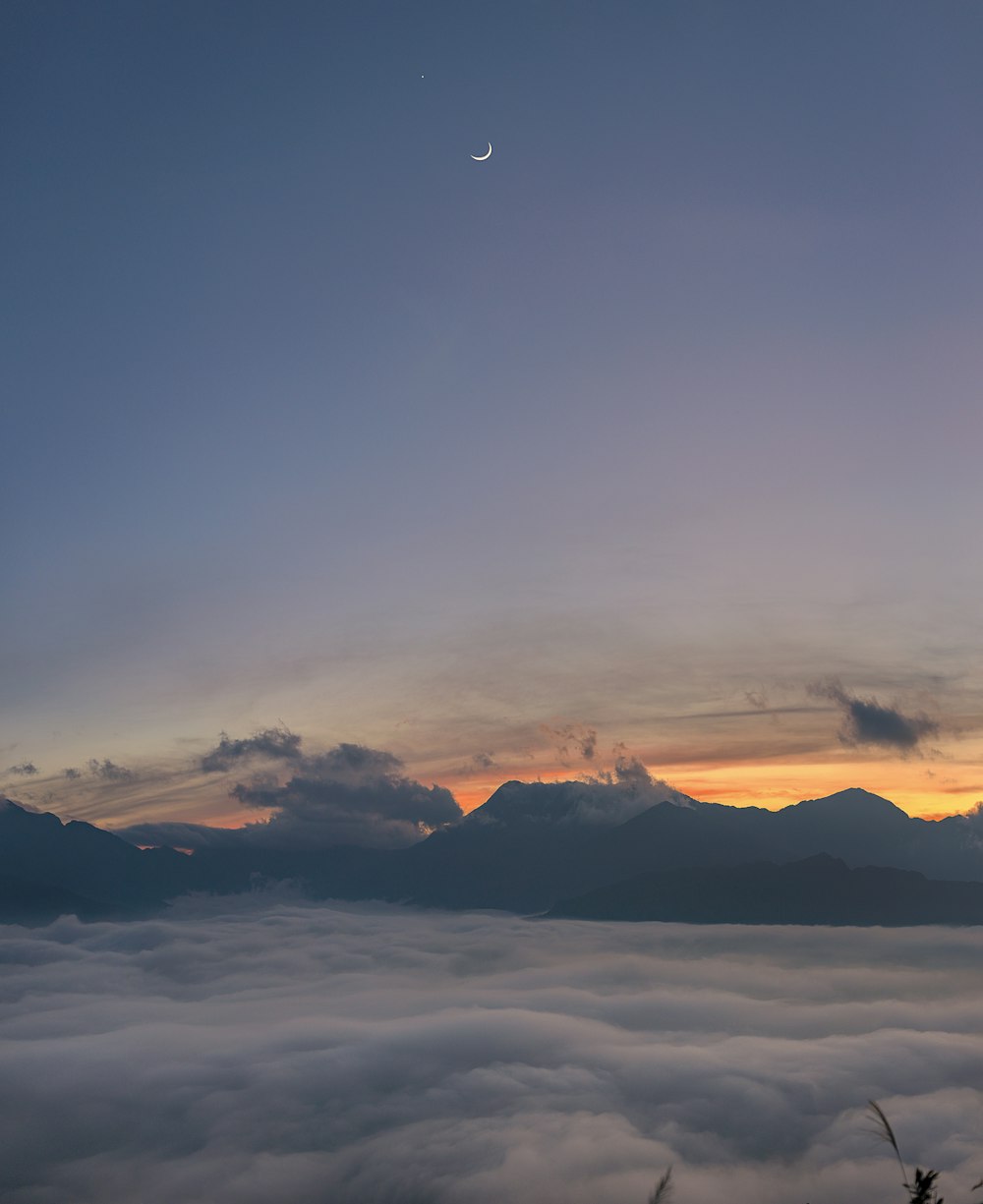 white crescent moon on blue sunset sky with clouds hovering below