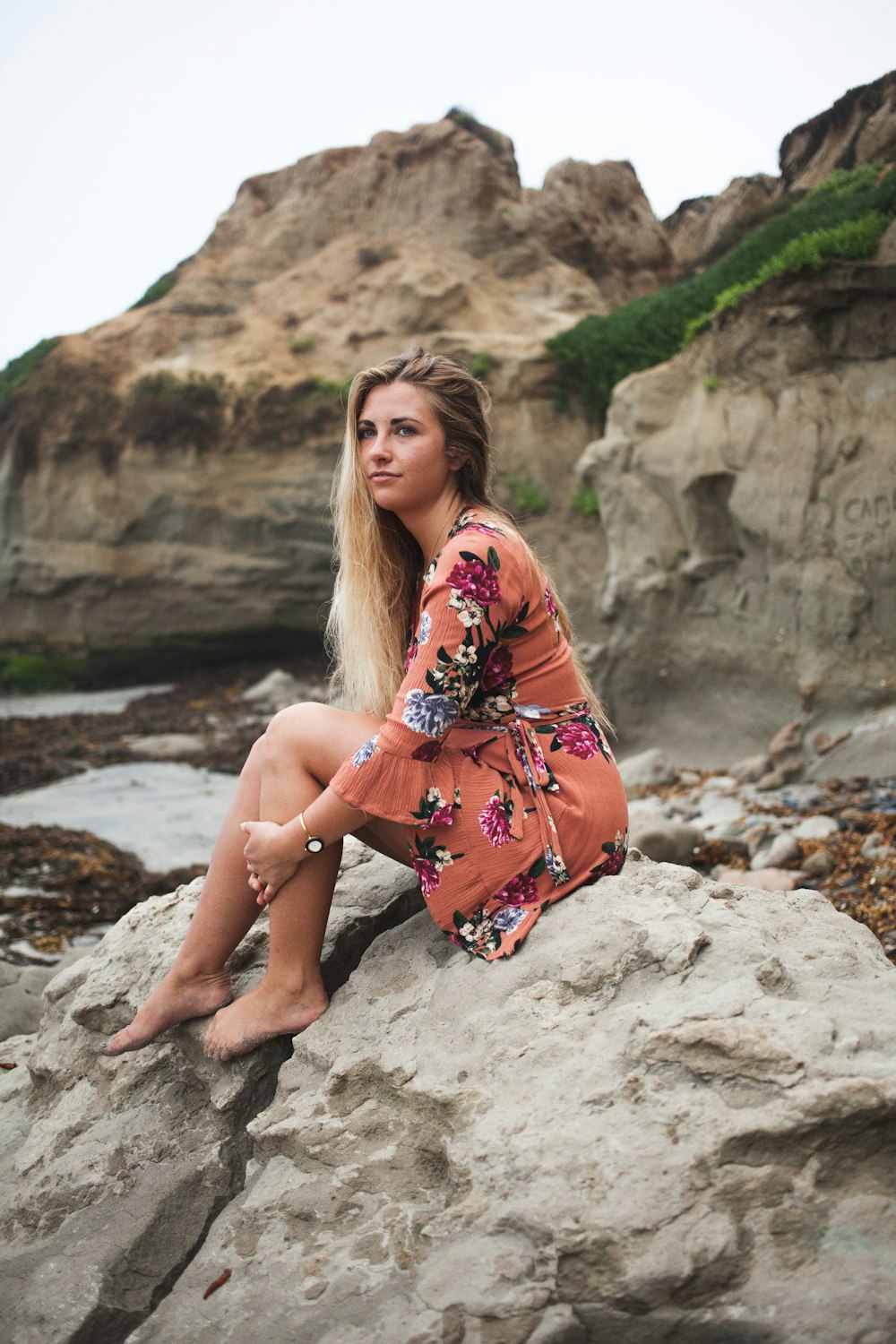 woman in pink and multicolored dress sits on rock