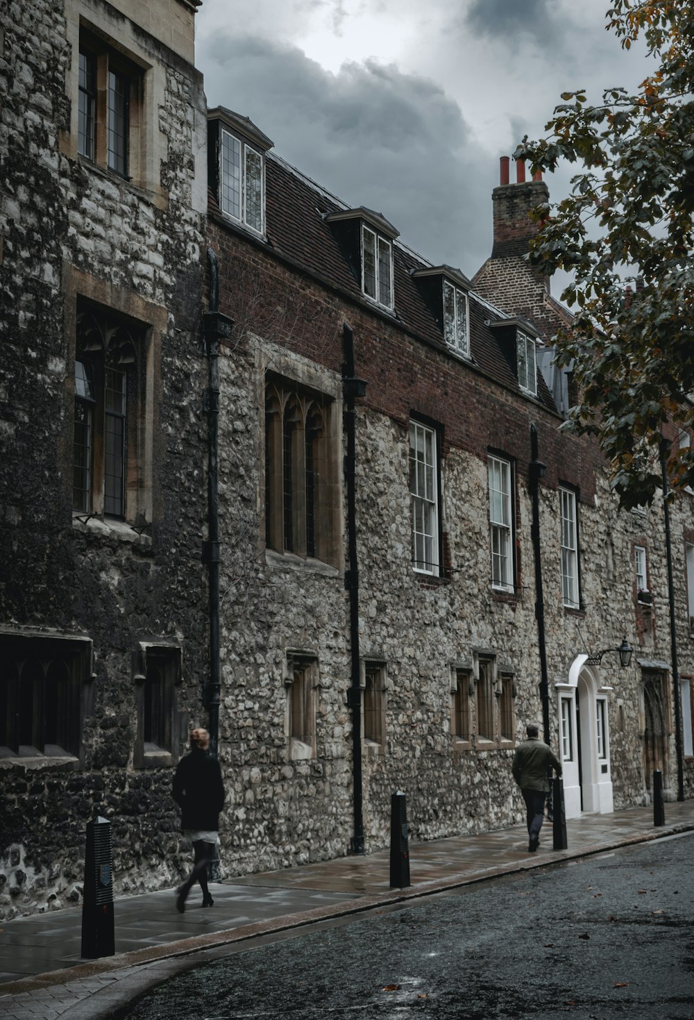 two people walks on sidewalk beside grey stone houses