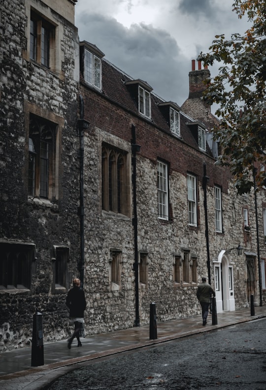 two people walks on sidewalk beside grey stone houses in Westminster Abbey Precincts - Dean's Yard United Kingdom