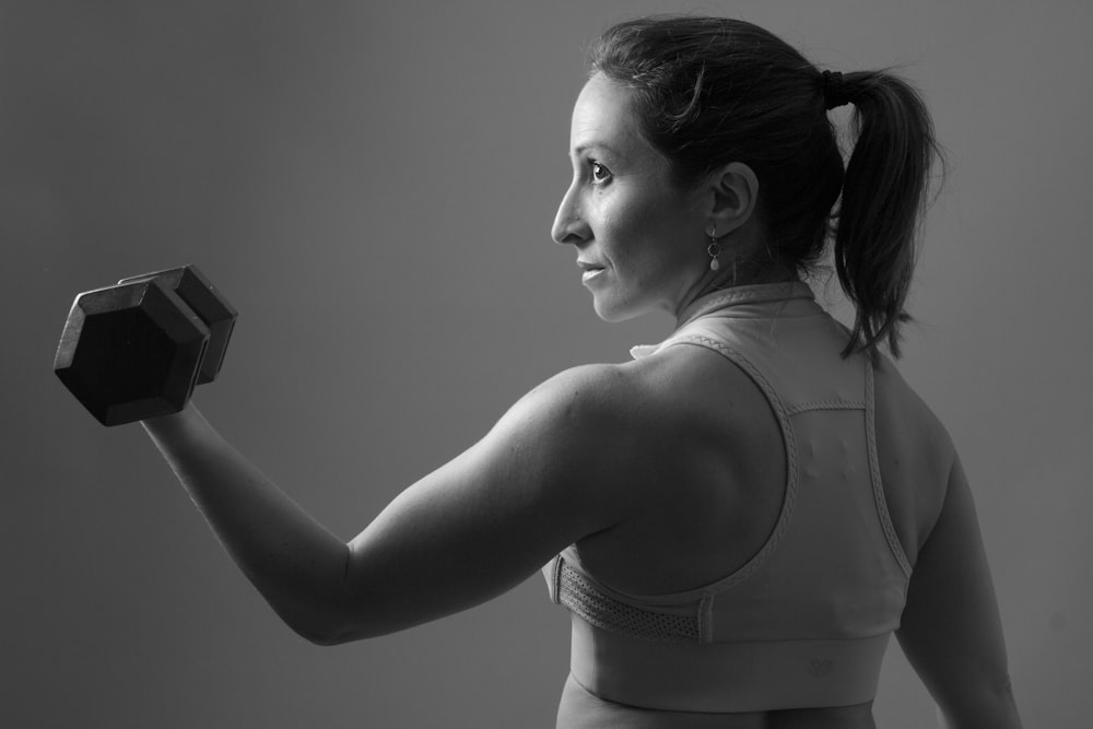 grayscale of woman carrying dumbbell