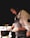 A chef wearing an apron and gloves is focused on preparing a dish in a dimly lit kitchen. The chef holds a pot over a plate, carefully arranging the food. The atmosphere is intimate and concentrated, emphasizing the art and skill of culinary creation.