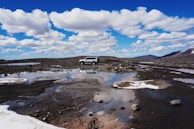 Close-up of a 4WD jeep parked on volcanic rocks with mountain backdrop.