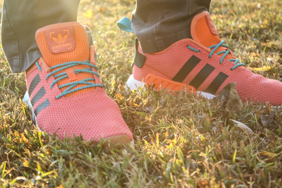 person wearing pair of pink-and-orange adidas low-top sneakers