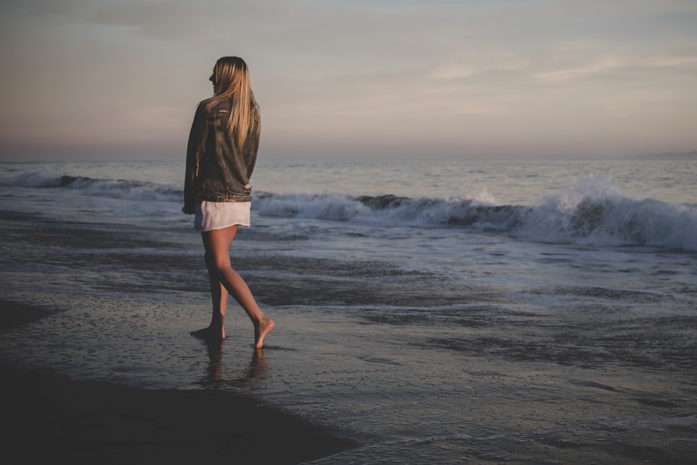 灰色の空の下で海岸を歩く女性
