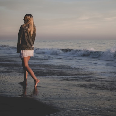 woman walking on seashore under gray sky