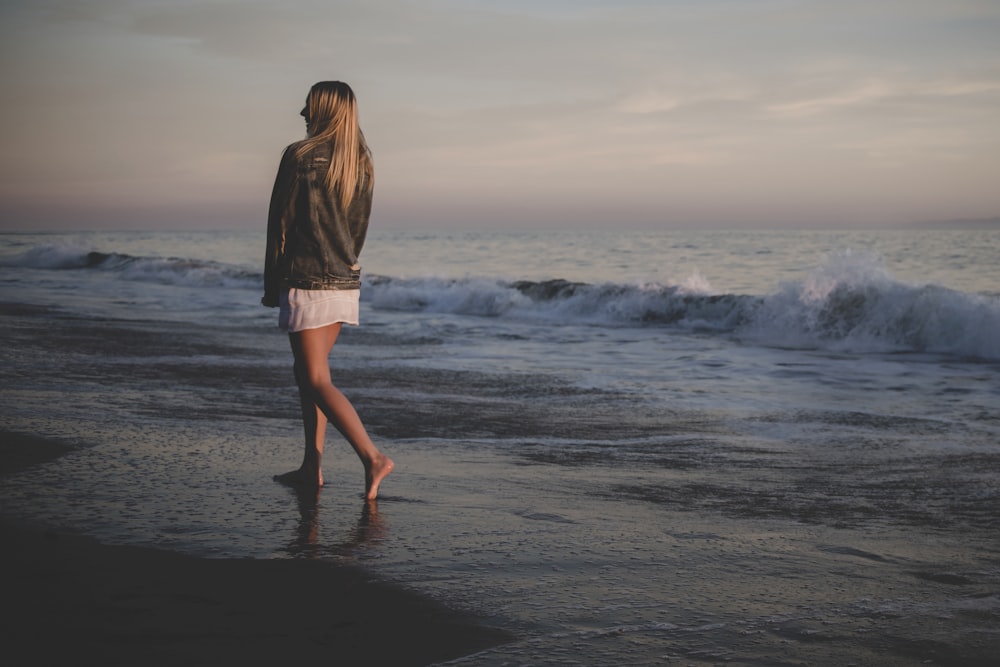 mulher que caminha na praia sob o céu cinzento