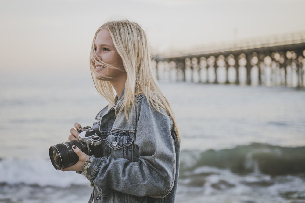 woman holding camera standing on seashore