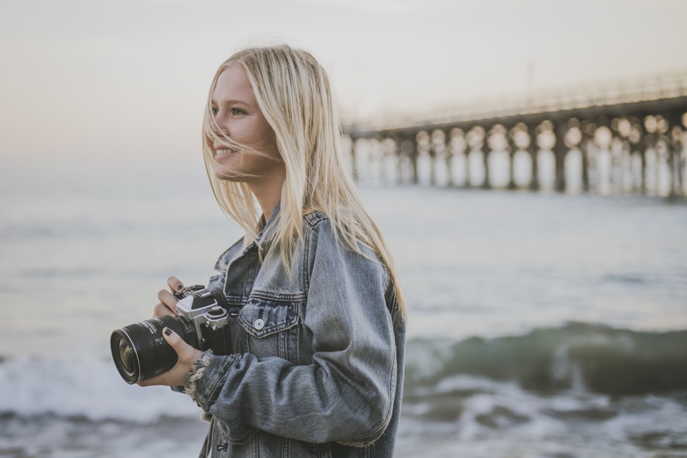 donna che tiene la macchina fotografica in piedi sulla riva del mare