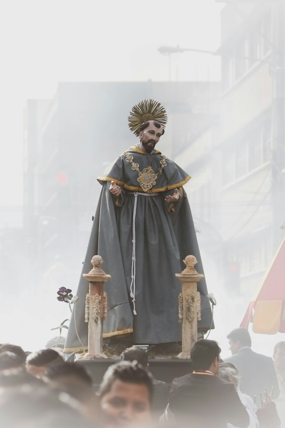 uomo in abito grigio e giallo statuetta religiosa che viene trasportato dalla gente