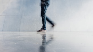 person wearing blue denim jeans beside gray wall
