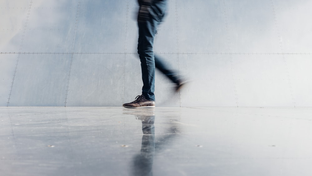 person wearing blue denim jeans beside gray wall