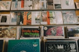 A collection of vinyl records is neatly organized on shelves. The records feature colorful and varied cover art, showcasing different music genres such as soul, funk, and hip hop. The record sleeves are arranged in rows, with some covers displaying artwork and text that are prominent and visually engaging.