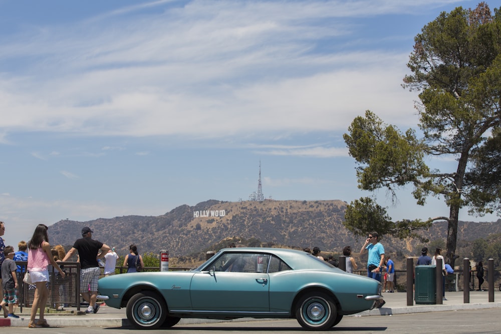 classic blue coupe on road beside people at near Hollywood sign at California during daytime