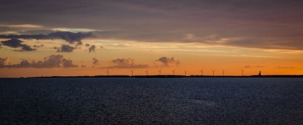 Un groupe de moulins à vent au loin avec un coucher de soleil en arrière-plan