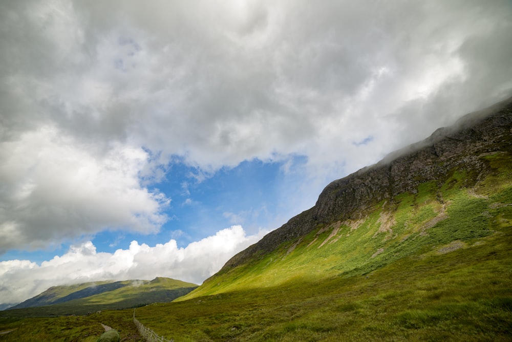 graue Wolken über dem mit grünen Gräsern bedeckten Tal