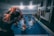 A group of individuals is engaged in a water aerobics class in an indoor swimming pool. The instructor, wearing a wristwatch, is demonstrating a stretch with their arms lifted over their head. Several participants in the pool are following the instructor’s lead, with their arms similarly raised. Colorful pool noodles are scattered along the poolside. Various towels hang on the wall of the pool area.