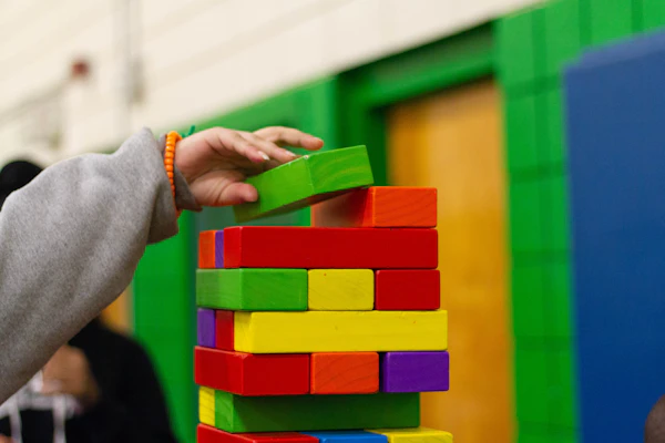 A little hand stacking a tower of rainbow building blocks