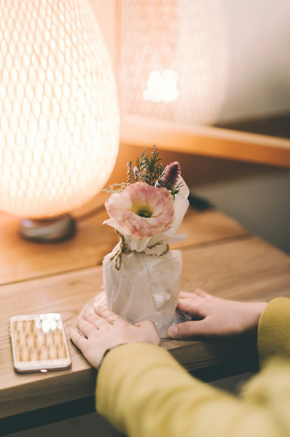 Persona que sostiene flores blancas y rosadas en maceta sobre mesa