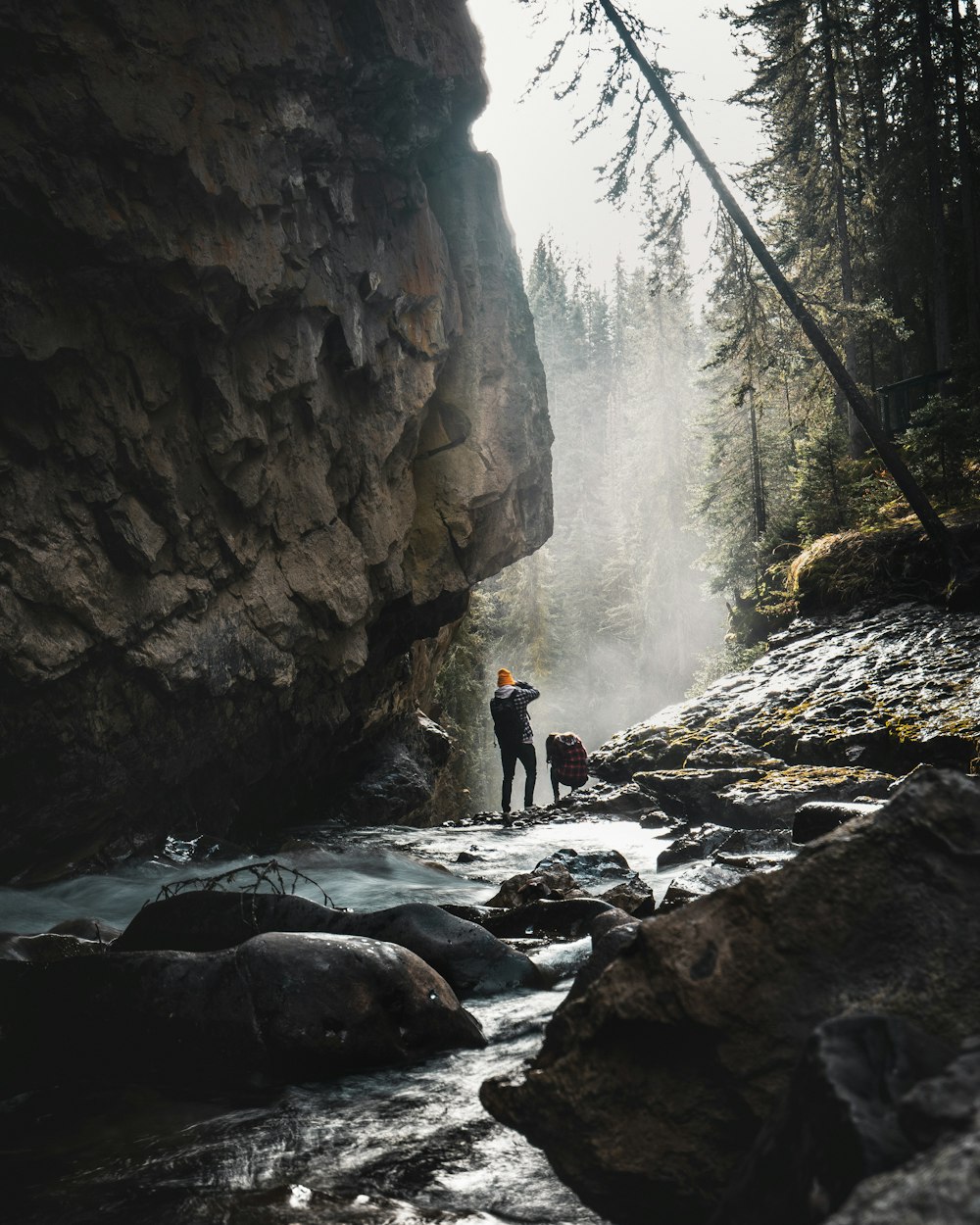 Hombre de pie en el río rocoso bajo el acantilado