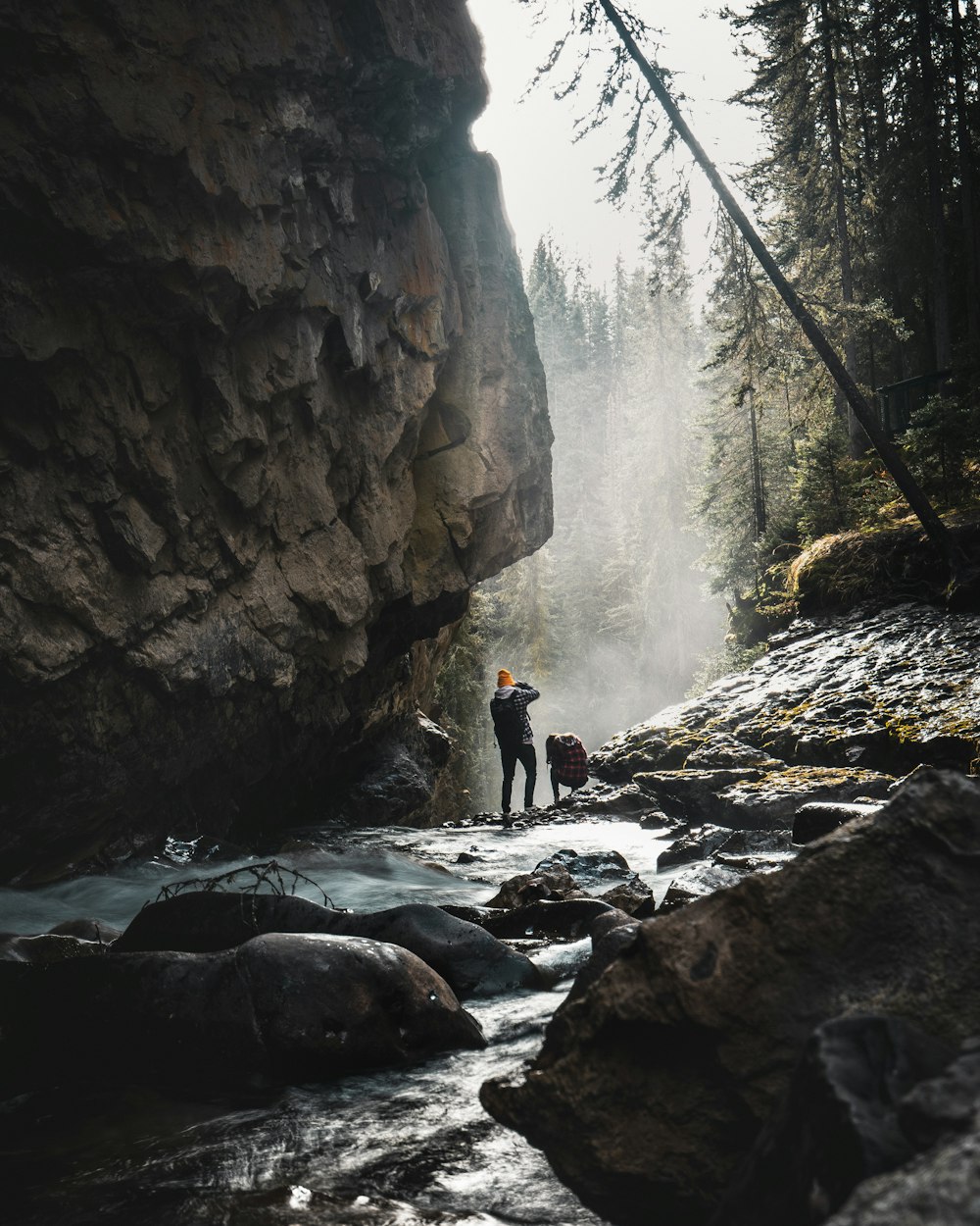 man standing on rocky river under cliff