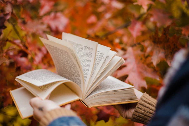 An open book with pages fluttering in the breeze, set against a backdrop of autumn leaves.