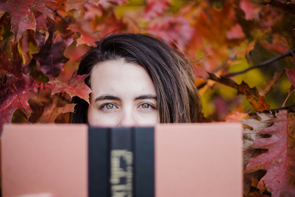 woman covering her mouth by book during daytime
