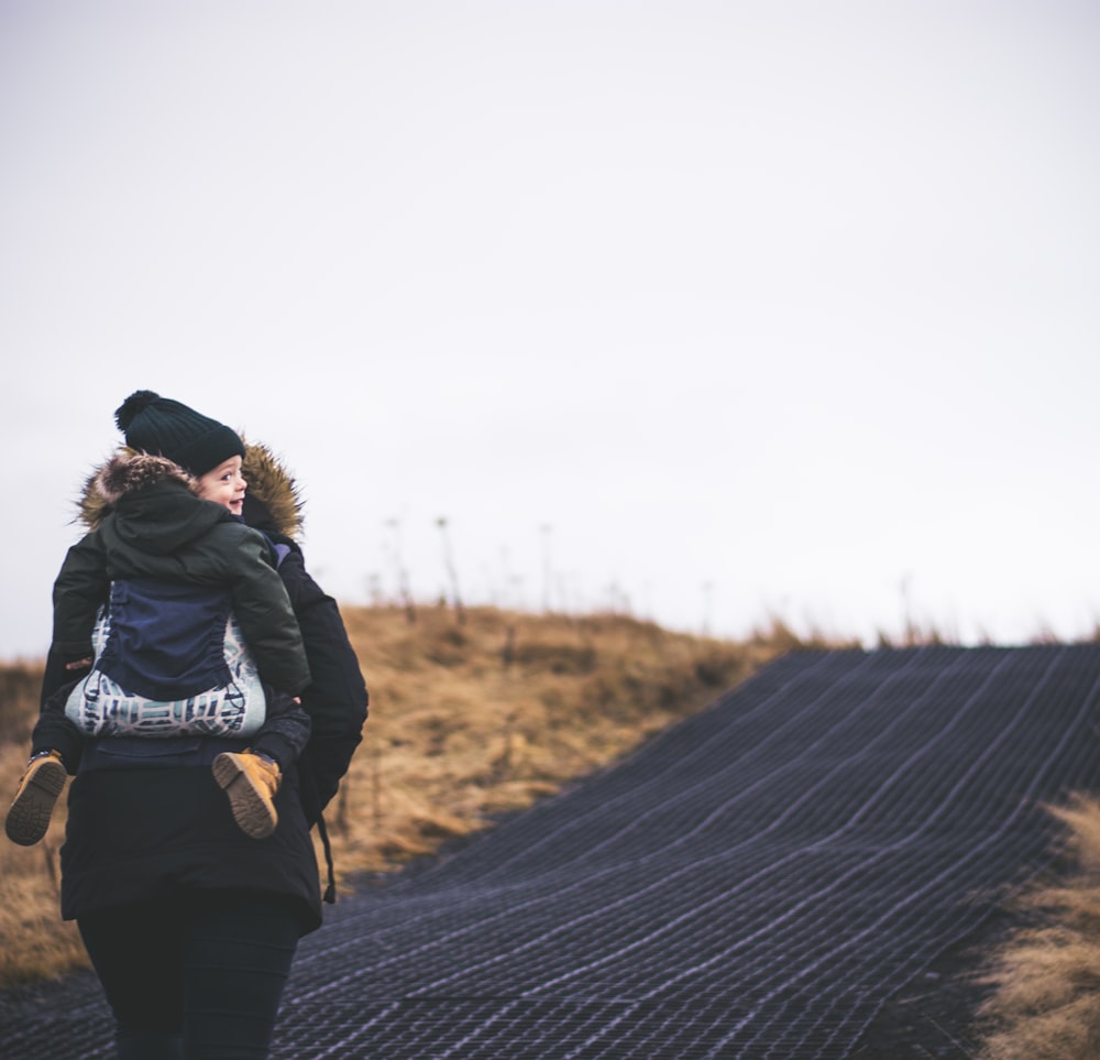 woman carries child piggy back on blacktop road