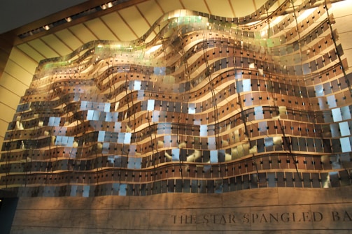 An architectural installation displays a wave-like pattern composed of metallic and reflective panels. The arrangement creates a sense of movement and fluidity, with patterns of light and shadow contributing to the dynamic appearance.