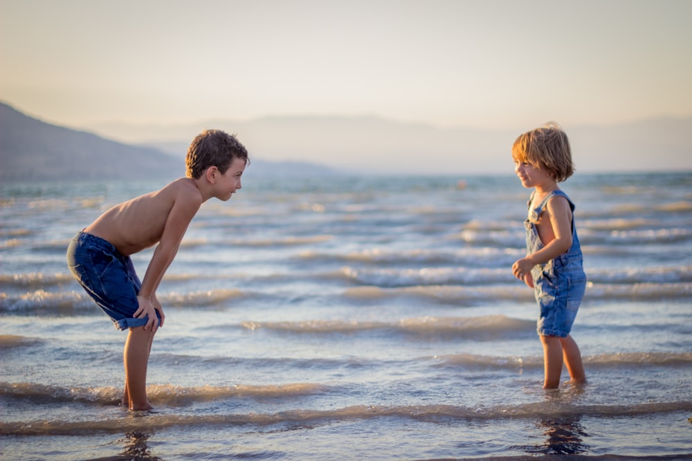 Junge beugt Knie, während er jüngeres Kind am Strand beobachtet