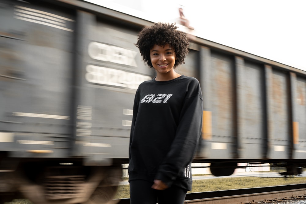 smiling woman in black sweater stands beside passing train