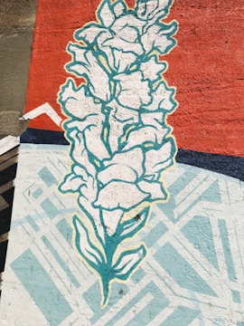 A mural features a stylized depiction of a white flower with blue-green outlines against a vibrant red background. Geometric patterns in light blue and white are interspersed, adding an abstract element to the composition.