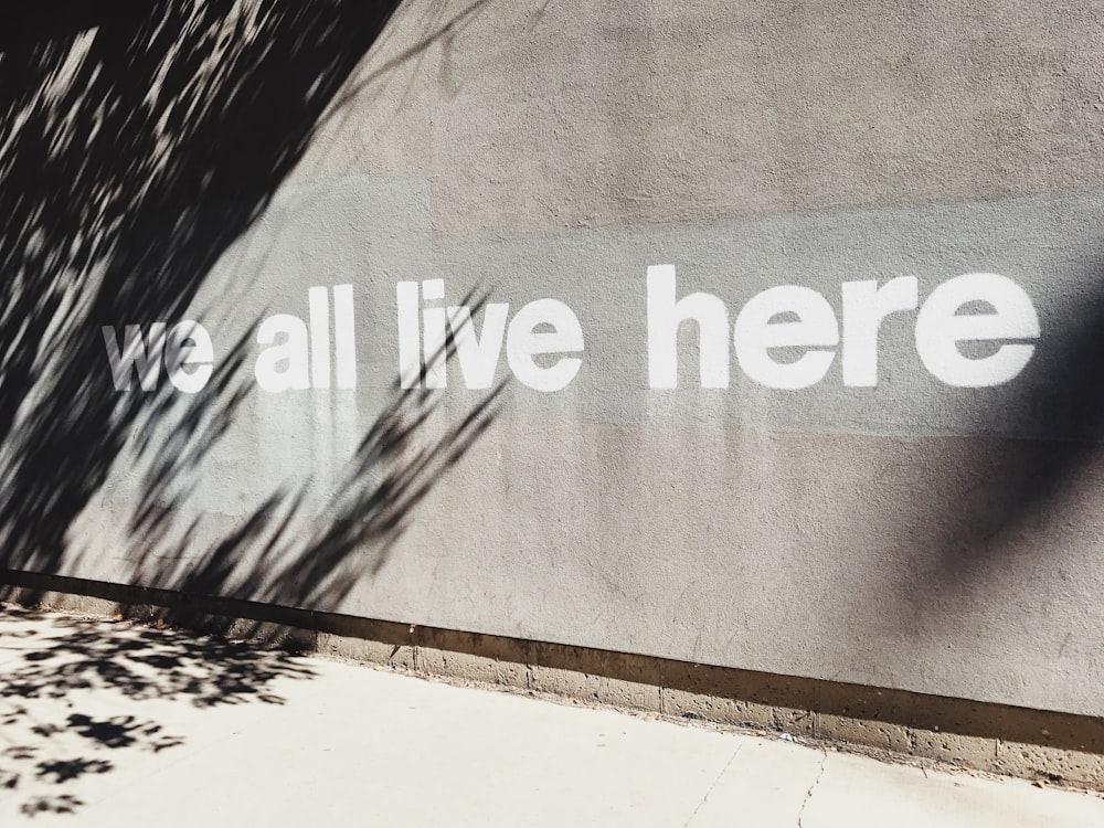 gray wall with we all live here graffiti