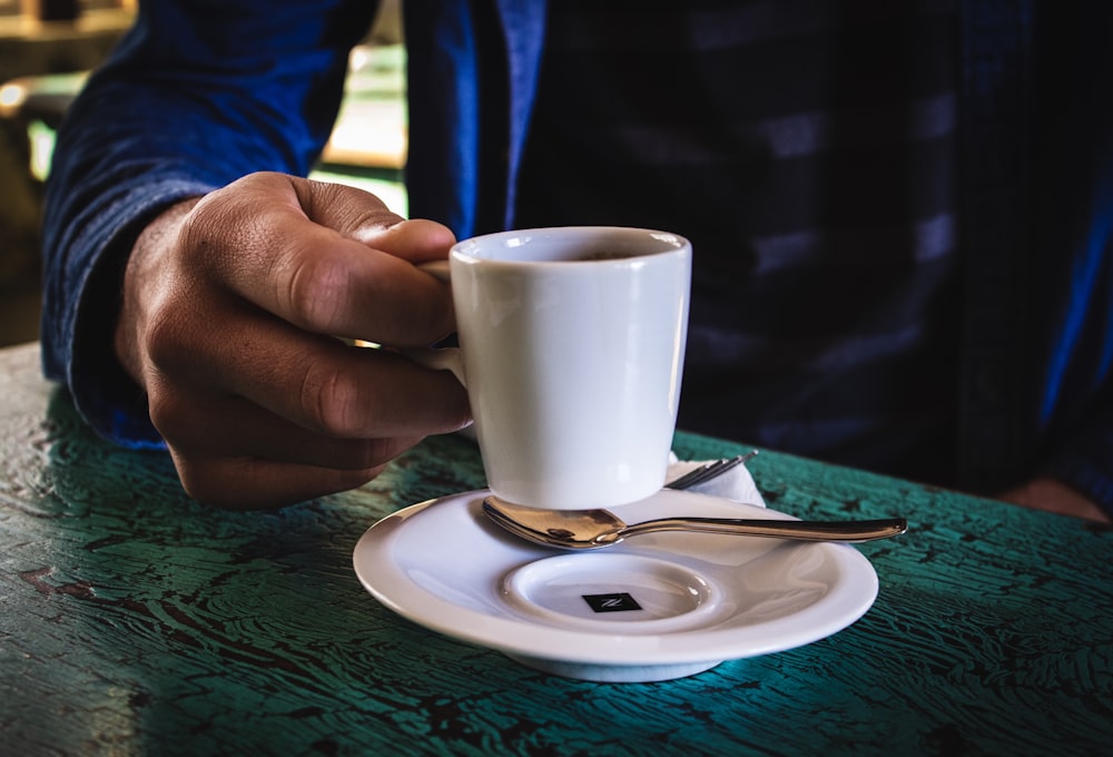 Persona sosteniendo una taza de cerámica blanca en el platillo