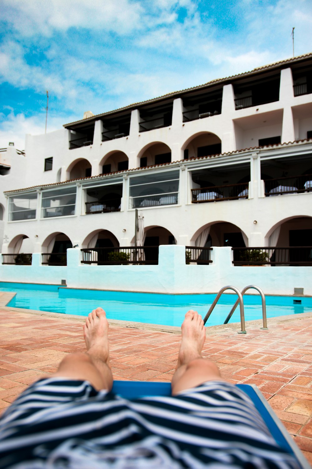 person lying on outdoor lounge chair near swimming pool